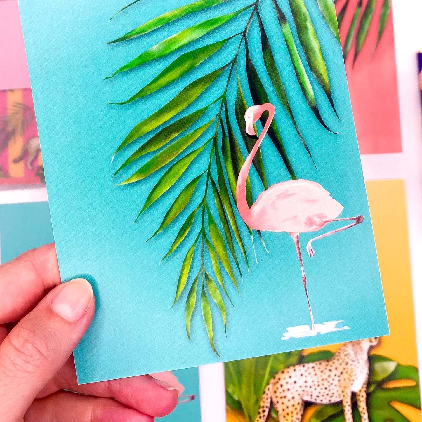 Close up of a pink flamingo and a palm leaf on a turquoise postcard by Jack & Orla