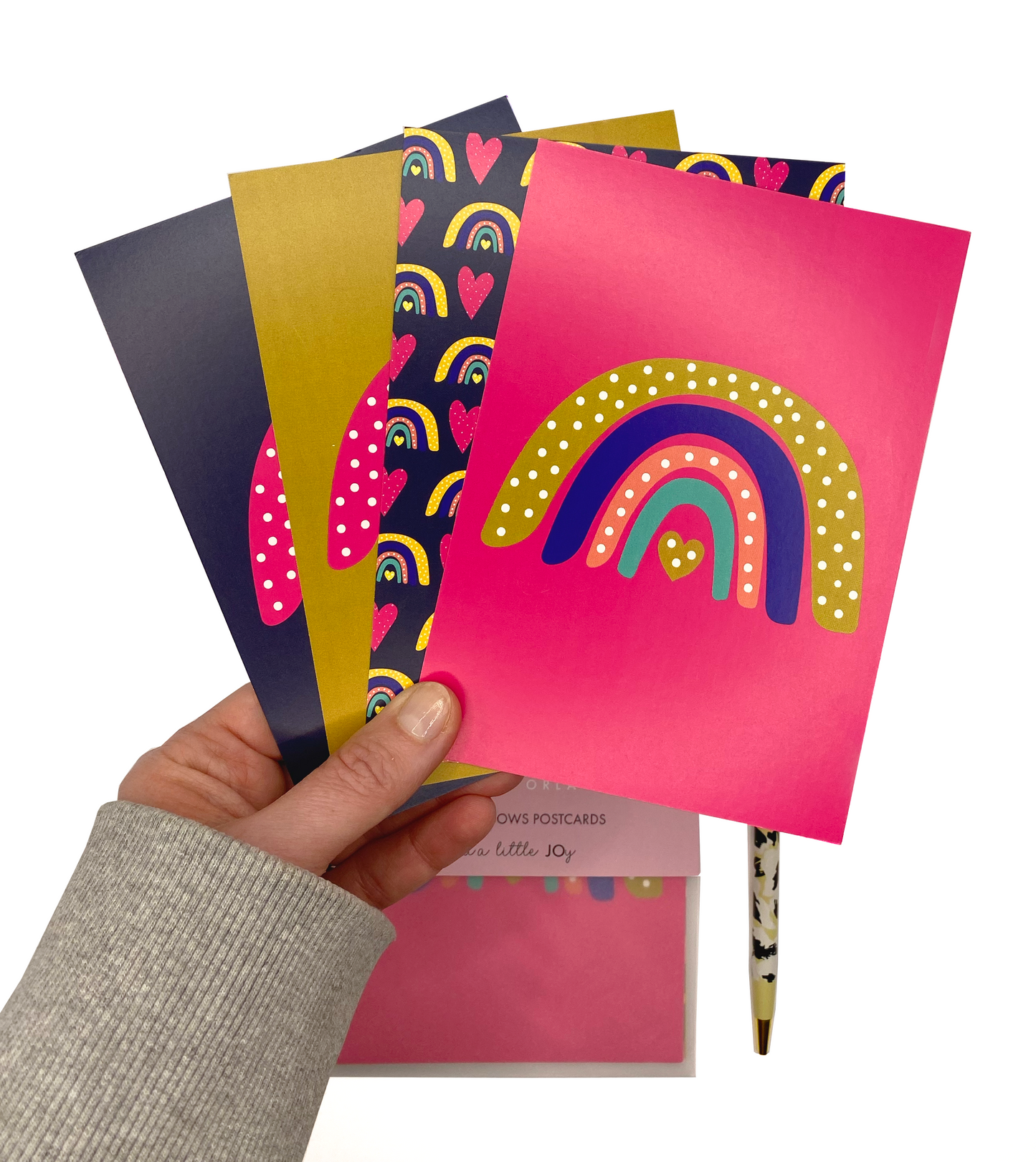 A hand holding a set of 4 rainbow postcards. The postcards are very bright and bold, in magenta, navy blue and mustard.