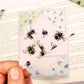 A close up of a hand holding an origami insect bookmark with a book in the background