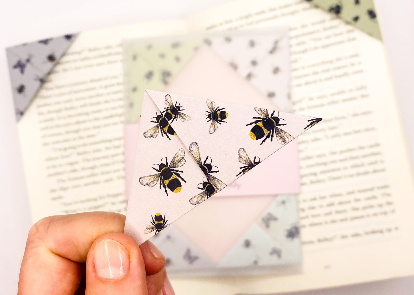 A close up of a hand holding an origami insect bookmark with a book in the background