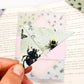 A close up of a hand holding an origami insect bookmark with a book in the background