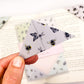 A close up of a hand holding an origami insect bookmark with a book in the background