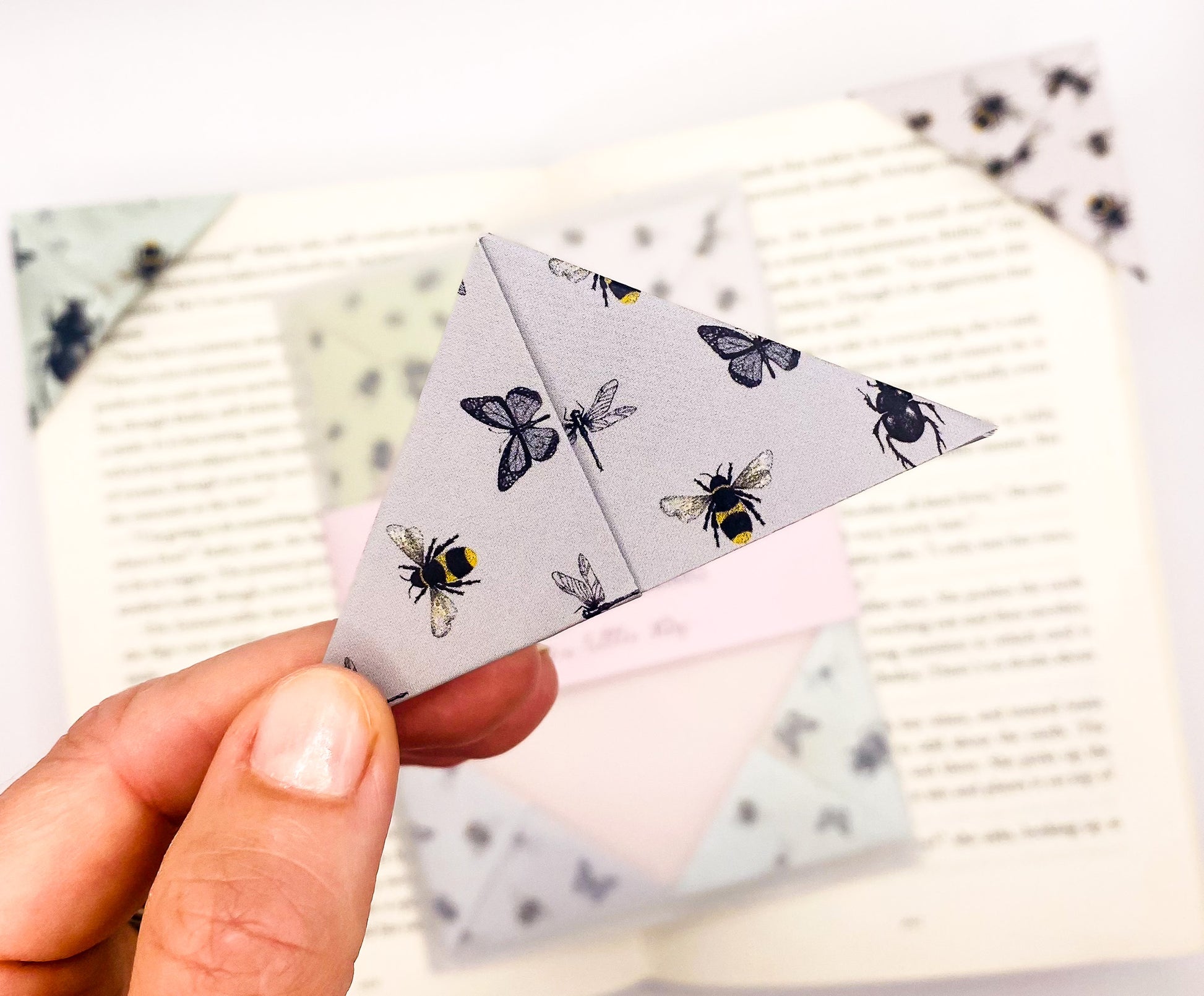 A close up of a hand holding an origami insect bookmark with a book in the background