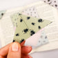 A close up of a hand holding an origami insect bookmark with a book in the background