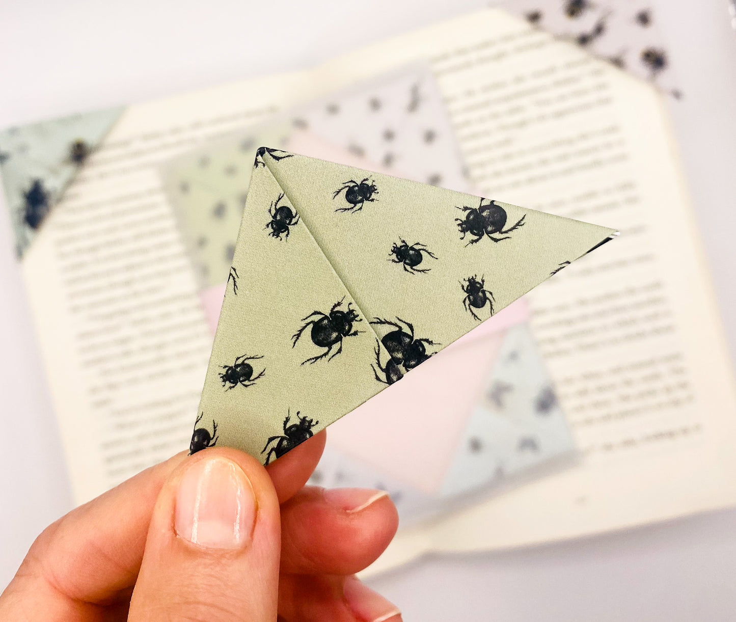 A close up of a hand holding an origami insect bookmark with a book in the background