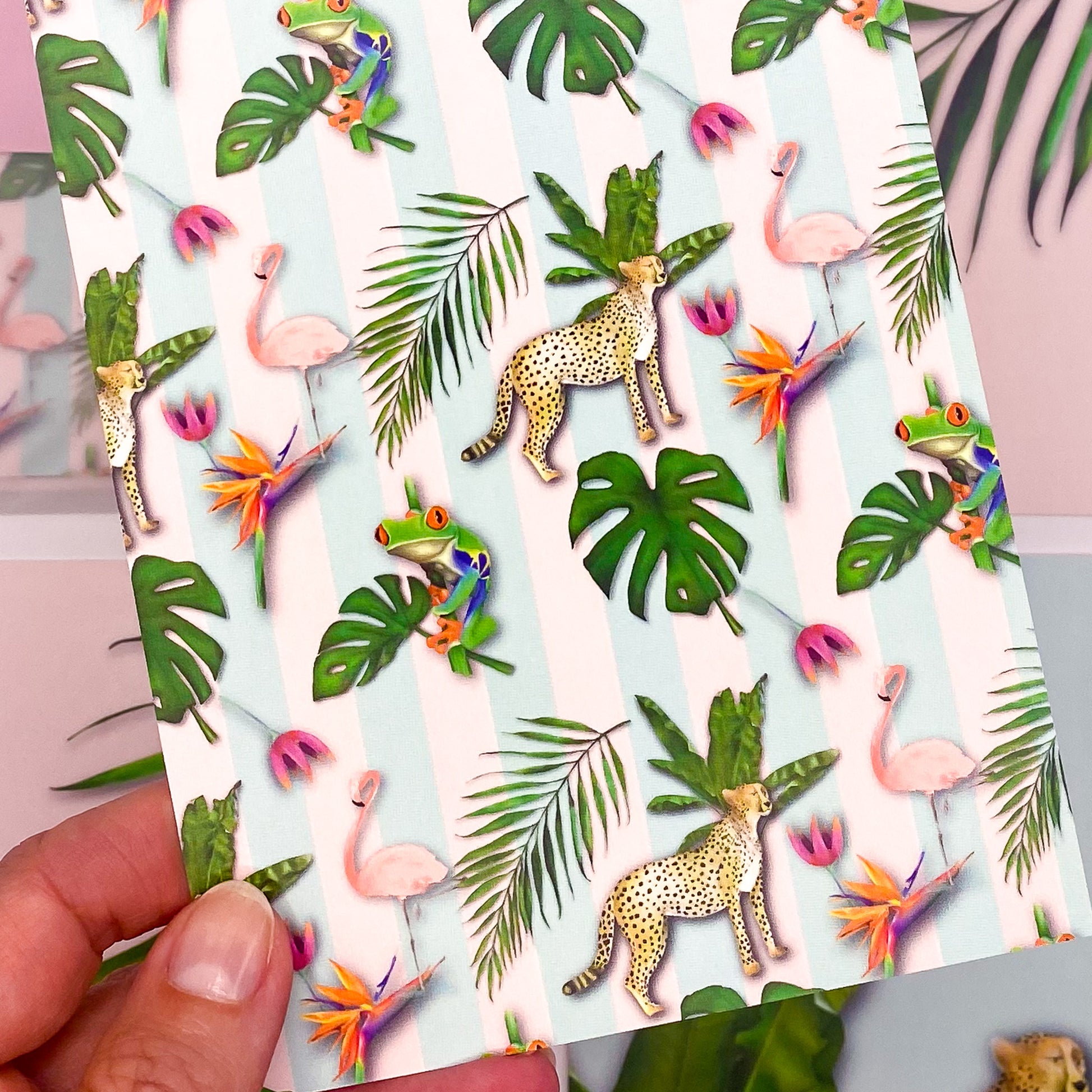 Close-up of pastel tropics postcard featuring cheetahs, tropical frogs, flamingos and palm leaves by Jack & Orla