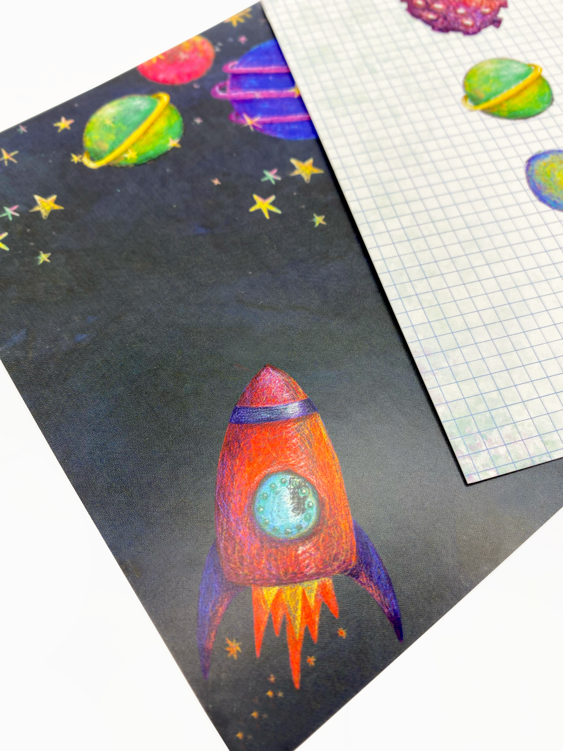 Close up image of two postcards in the space collection. The postcard in the foreground features a navy background with stars, planets and a red rocket.