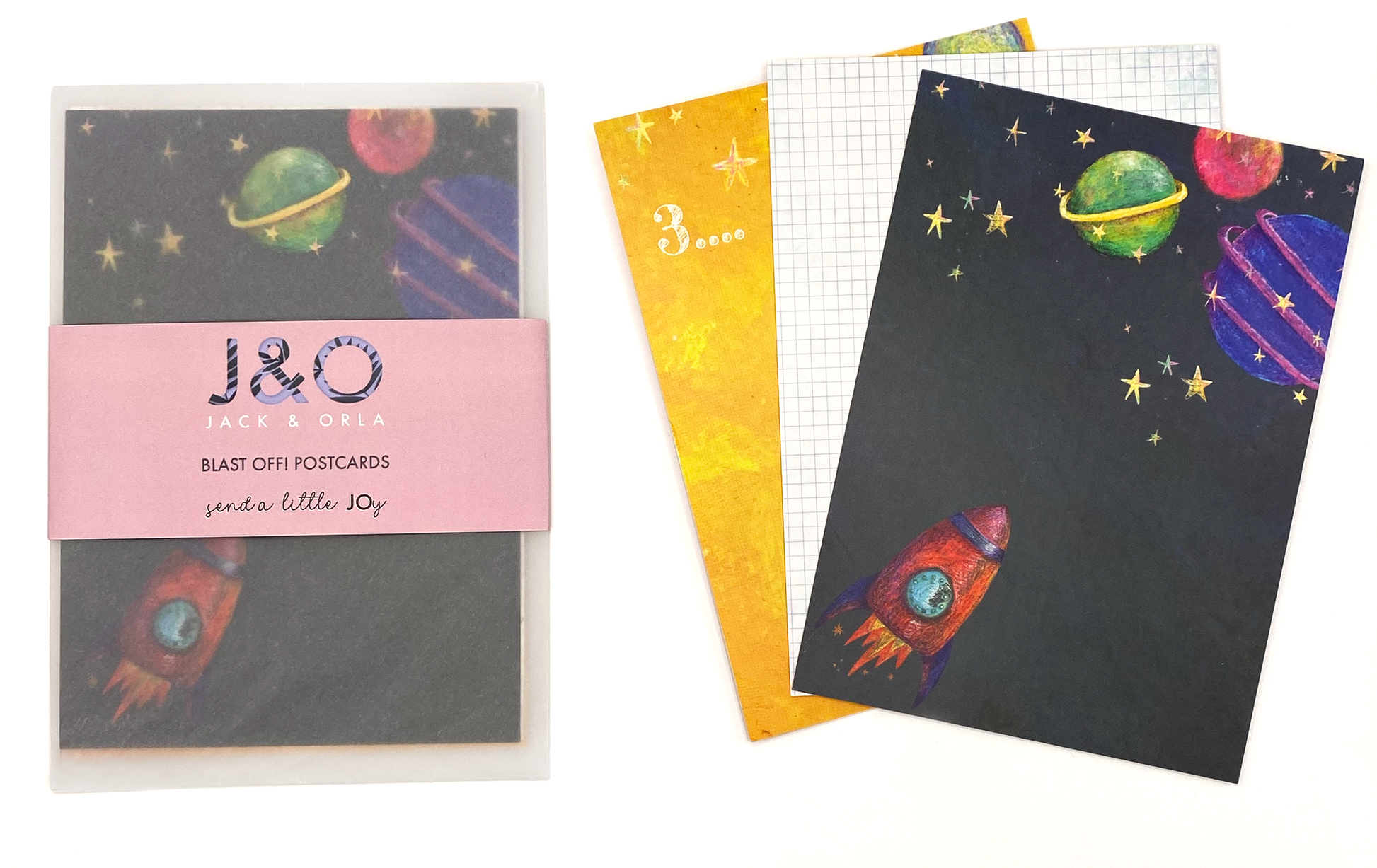 A photo featuring three of the designs in the space themed postcard gift set, as well as a packaged set. The front postcard has a navy background with stars, brightly coloured planets and a red rocket.